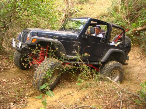 2001 Jeep Wrangler - A black 2001 Jeep Wrangler navigates an off-road trail with visible red suspension components.