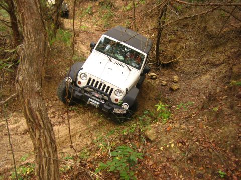 2001 Jeep Wrangler - A white Jeep Wrangler navigates a steep, wooded trail, with another vehicle partially visible behind it.