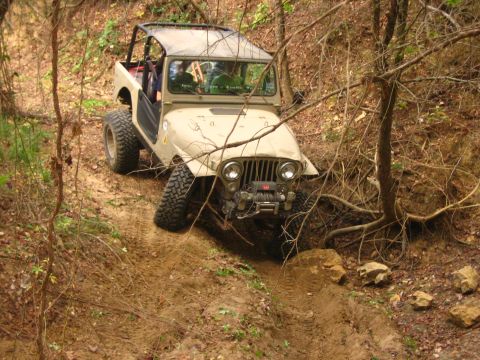 2001 Jeep Wrangler - A tan Jeep CJ-7 navigates a steep, wooded trail with large tires.