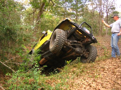 2001 Jeep Wrangler - A yellow 2001 Jeep Wrangler is overturned on a wooded trail, with a man observing the scene.