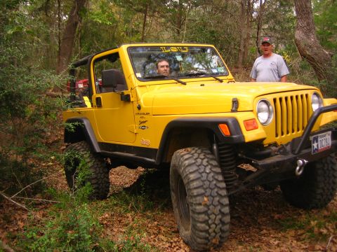 2001 Jeep Wrangler - A yellow 2001 Jeep Wrangler is parked on a dirt trail surrounded by trees, with two men visible.
