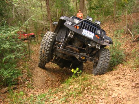 2001 Jeep Wrangler - A black 2001 Jeep Wrangler navigates a challenging off-road trail, while another red Jeep is visible further down the path.