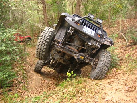 2001 Jeep Wrangler - A Jeep Wrangler is tilted on its side on a wooded trail, with another vehicle in the background.