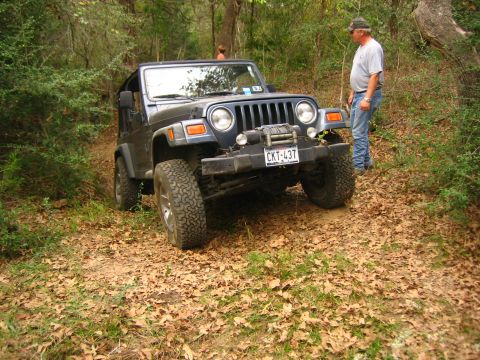 2001 Jeep Wrangler - A blue 2001 Jeep Wrangler navigates a wooded trail, equipped with a winch for off-road challenges.