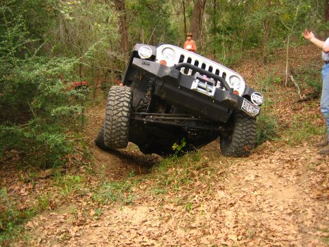 2001 Jeep Wrangler - A Jeep Wrangler navigates a steep, wooded trail with one wheel lifted off the ground.