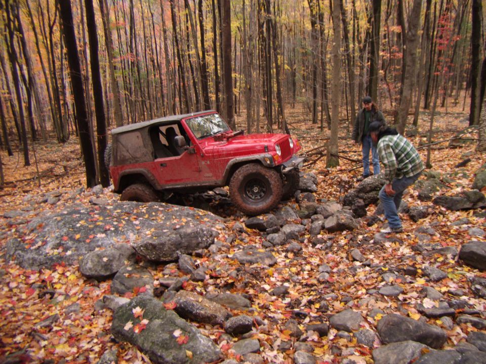 2003 Jeep Wrangler navigating a rocky trail in a forest during autumn