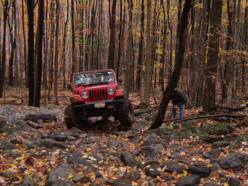 Red Jeep Wrangler on rocky terrain in autumn forest