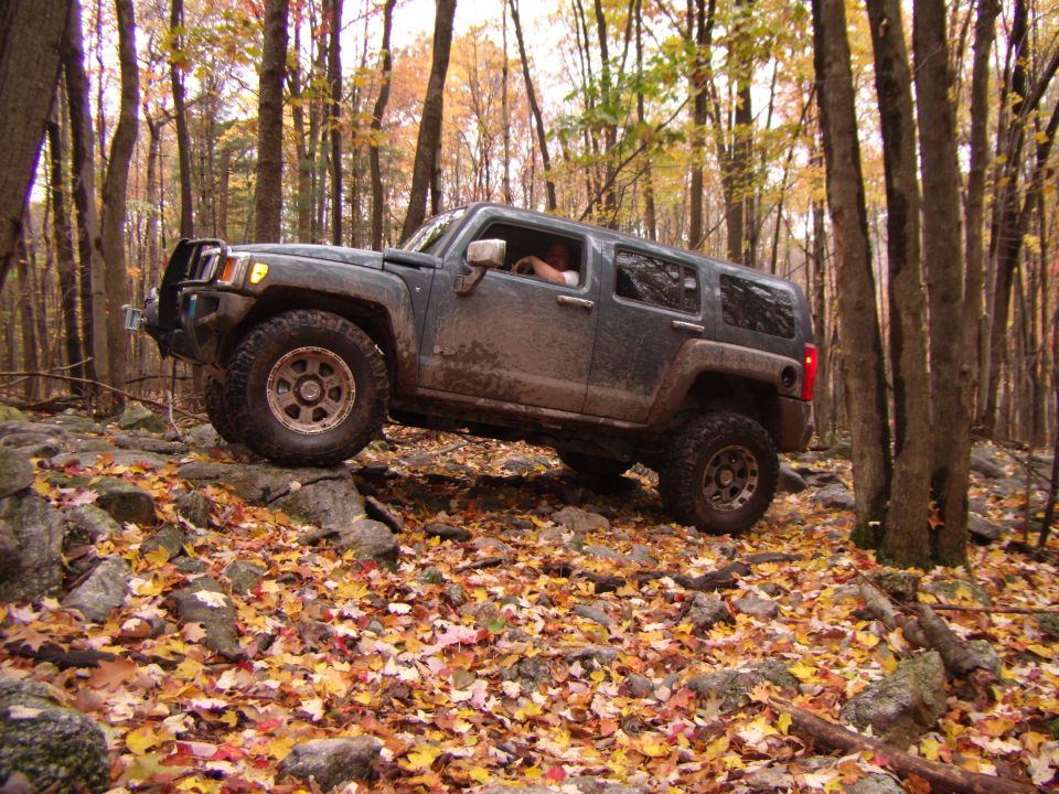 Dark SUV navigating rocks on a forest trail in autumn. This is a Hummer H3