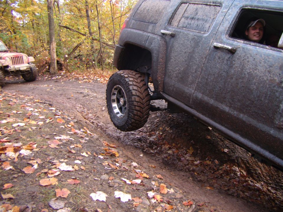 Hummer H3 driving on a muddy trail with one wheel off the ground. Another Jeep is visible in the background