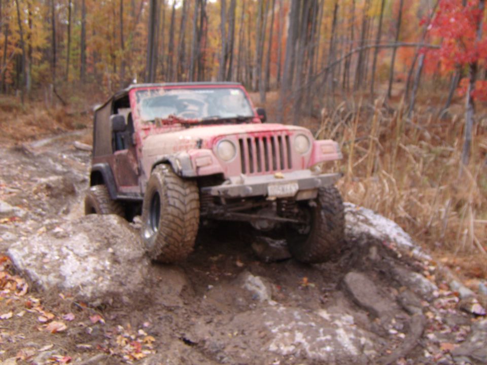 Red 2003 Jeep Wrangler on a muddy, rocky trail with fall foliage