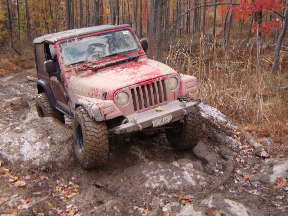 Red 2003 Jeep Wrangler navigating a rocky, muddy trail