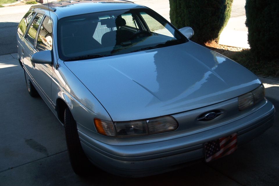 Silver Ford Taurus wagon parked in driveway, front three-quarter view with American flag front plate