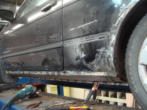 1996 Ford Bronco - Rocker panel rust repair in progress on a black car, with welding equipment visible.