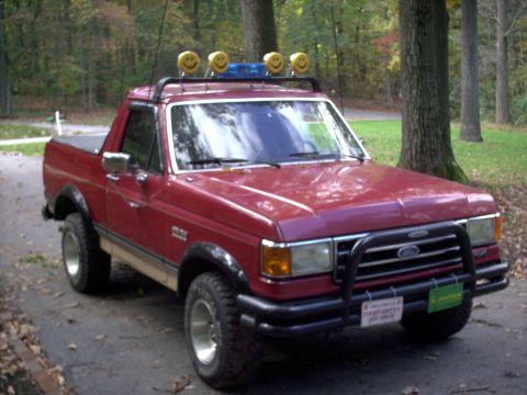 1989 Ford Bronco - This red pickup truck has a custom roof rack with smiley face lights and a blue light bar.