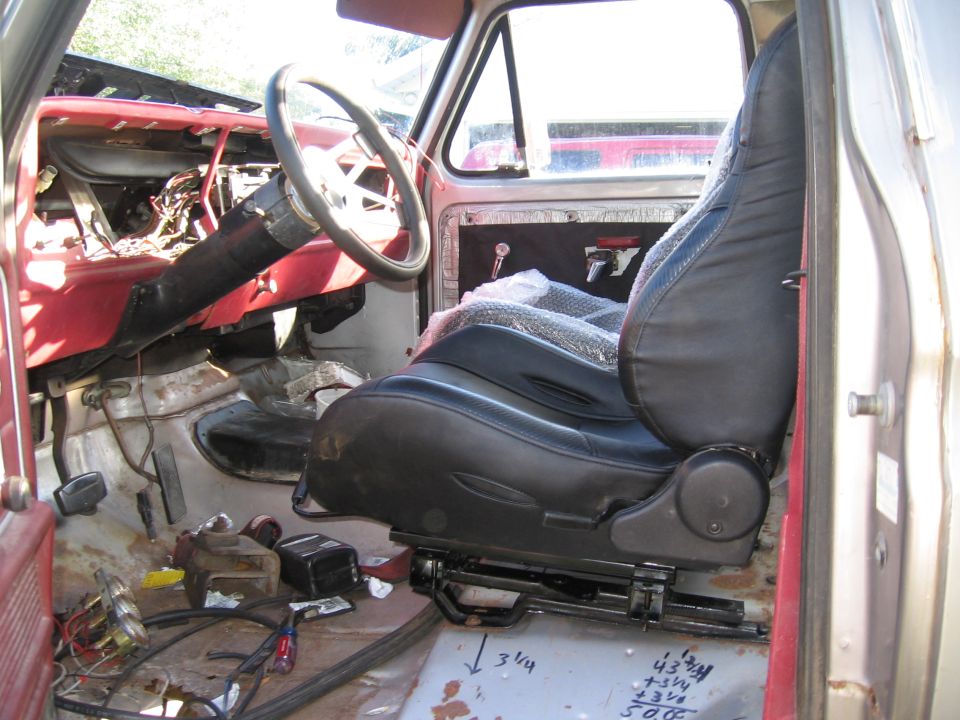 Interior of a 1979 Ford F-150 showing the driver's seat, dashboard, and steering column. The seat is covered in plastic