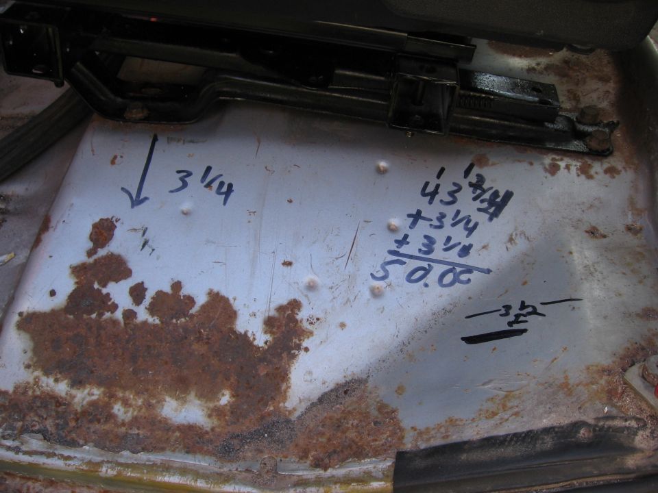 Close-up of a rusty vehicle floor with handwritten measurements and a math problem