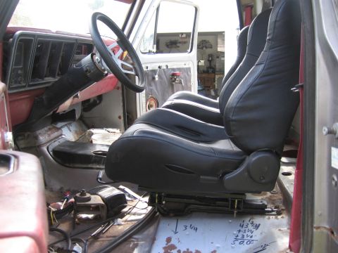 1979 Ford F-150 - Black aftermarket bucket seat mounted in a bare, rusty truck cab with exposed floor and red door panel.