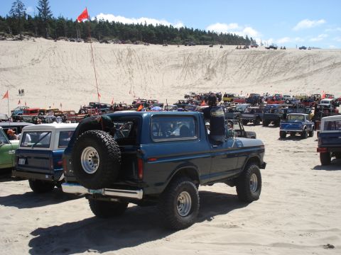 1979 Ford Bronco - Several vehicles gathered at a sandy location, with a dark blue Ford Bronco in the foreground.
