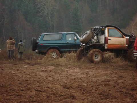 1979 Ford Bronco - Two off-road vehicles are stuck in the mud with trees in the background.