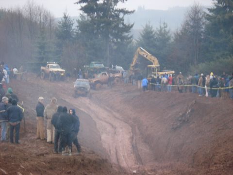 1979 Ford Bronco - Spectators watch as multiple off-road vehicles tackle a challenging mud track during an event.