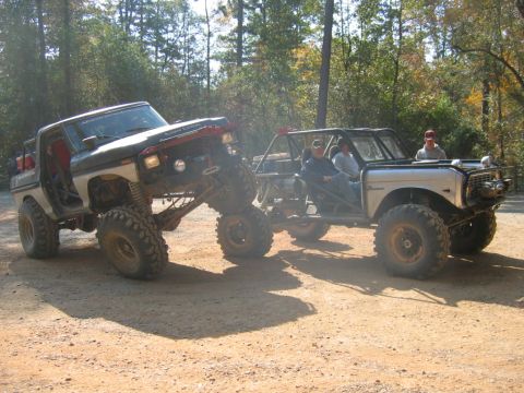 1992 Ford Mustang - Two custom off-road vehicles are parked on a dirt trail surrounded by trees.