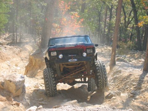 1992 Ford Mustang - An off-road vehicle navigates a challenging, dusty, and rocky trail through a wooded area.