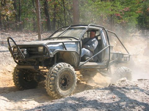 1992 Ford Mustang - Off-road pickup truck with extensive modifications and roll cage navigating a dirt trail.