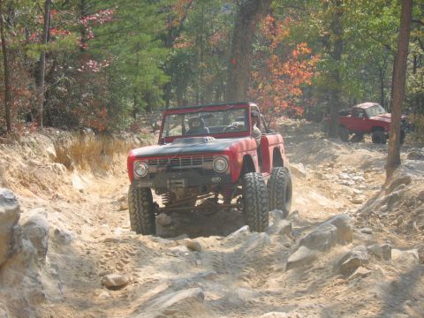 1992 Ford Mustang - Two off-road vehicles navigate a challenging, rocky path through a wooded area.