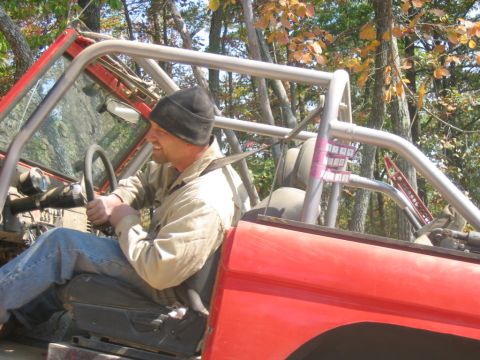 1992 Ford Mustang - Driver in a red off-road vehicle with a roll cage, seen from the side.