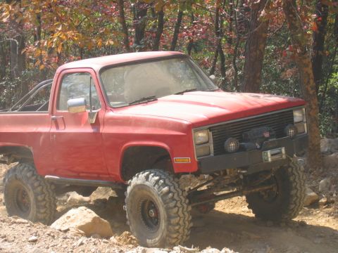 1992 Ford Mustang - Modified red pickup truck navigates a rocky off-road trail during autumn.
