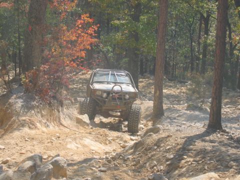 1992 Ford Mustang - An off-road vehicle navigates a challenging rocky trail surrounded by trees in autumn.