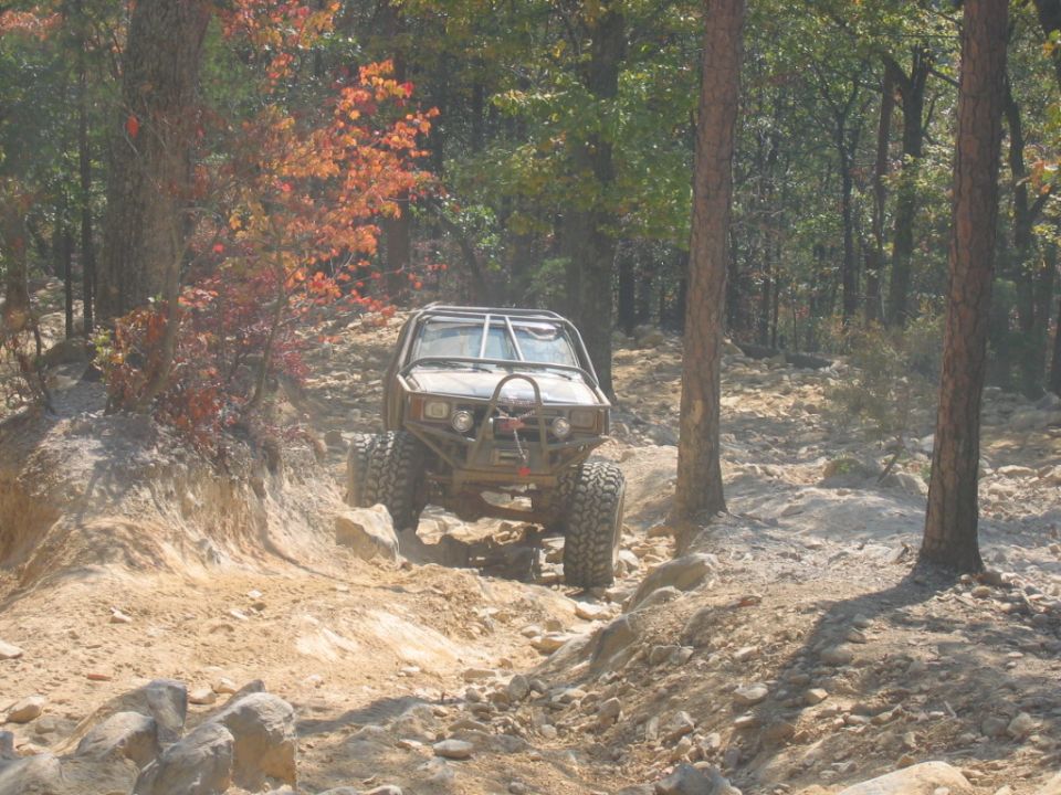 off-road vehicle with roll cage driving over rocks in a forest