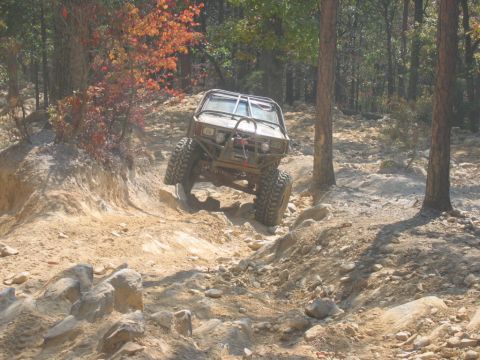 1992 Ford Mustang - An off-road vehicle navigates a challenging rocky terrain in a wooded area.
