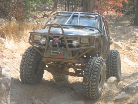 1992 Ford Mustang - Modified Toyota truck navigating a challenging off-road trail with a full roll cage.