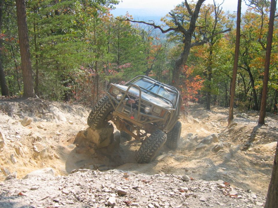 Off-road vehicle with large tires navigating a rocky incline on a wooded trail