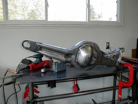 1996 Ford Bronco - A bare metal rear axle housing is clamped to a workbench, with tools like a sander and grinder nearby.