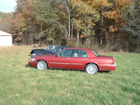 2001 Mercury Grand Marquis - A red 2001 Mercury Grand Marquis is parked in a field next to another vehicle.