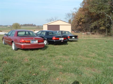 2001 Mercury Grand Marquis - Three Mercury Grand Marquis sedans are parked in a field on a clear day, with a barn and trees visible.