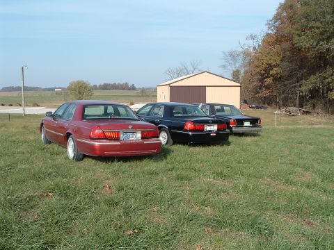 2001 Mercury Grand Marquis - Three sedans are parked in a grassy field near a barn.