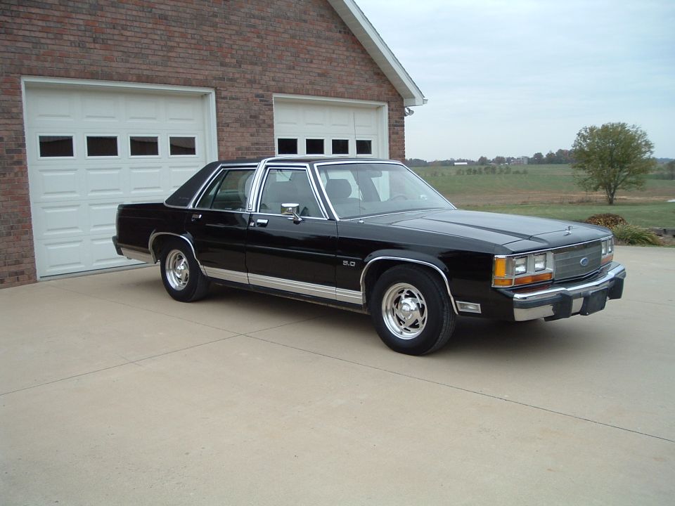 Black Ford LTD Crown Victoria sedan on a driveway in front of a brick garage