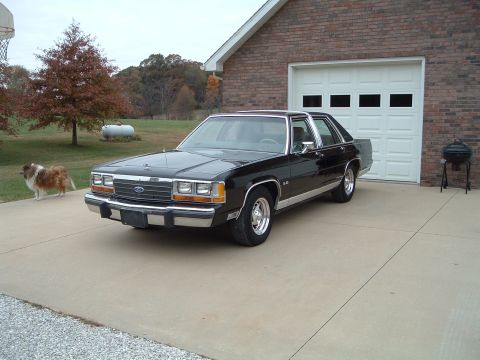 1989 Ford Crown Victoria LTD - A black 1989 Ford Crown Victoria is parked in front of a brick garage on a cloudy day.