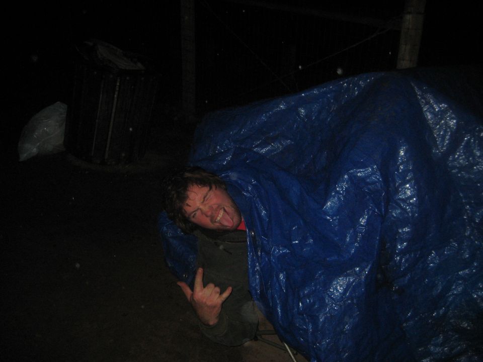 Person making a rock-on hand gesture and sticking out their tongue while under a blue tarp