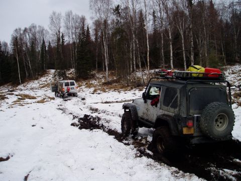 2000 Ford E350 - Two off-road vehicles navigate a challenging muddy and snowy path through a forest.