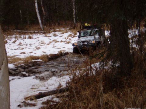 2000 Ford E350 - A silver Jeep Wrangler navigates a challenging off-road path covered in snow and mud.