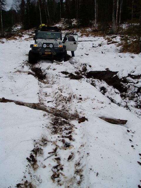 2000 Ford E350 - A silver Jeep Wrangler is stuck in a muddy, snowy track with its driver's door open.
