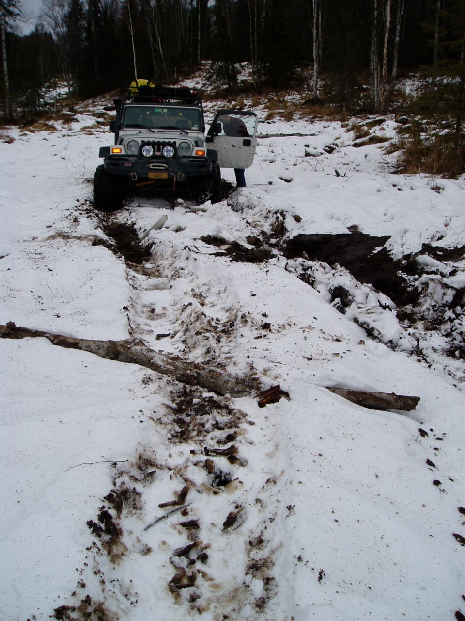 Silver Jeep Wrangler with open driver door stuck in snowy terrain, front view