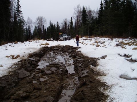 2000 Ford E350 - An off-road vehicle tackles a difficult path through mud and snow, with a person observing the challenging conditions.