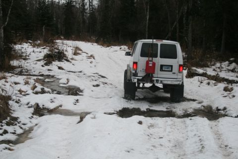 2003 Jeep TJ - White van navigates a snowy, wooded path with puddles and tire tracks visible.