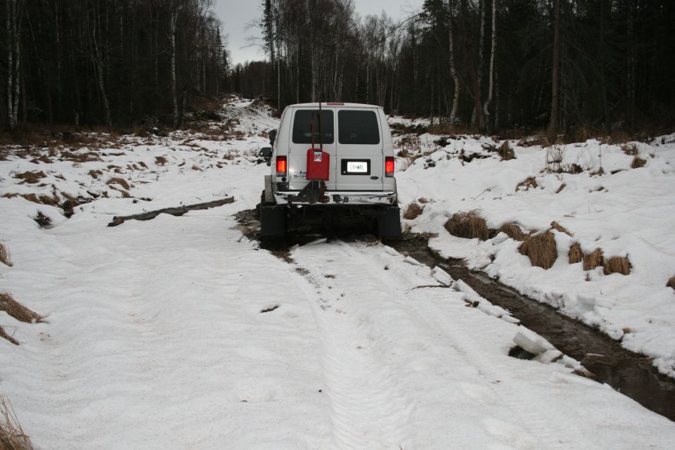 White van with a red gas can mounted on the rear, stuck in snow and mud