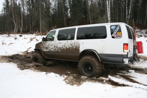 2003 Jeep TJ - A white van with large off-road tires navigates a muddy and snowy terrain, displaying an ARB sticker on its rear window.